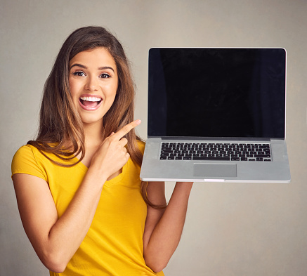 Shot of an attractive young woman holding a laptop with a blank screen against a grey background