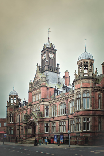 Magistrates Court in York. The building is an ornate red brick Victorian structure. On the pavement are commuters pasing in front of the building.
