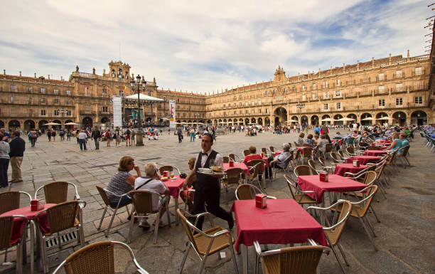 Waiter and other people walk on the historical Plaza Mayor,or main square, with tables and chairs of a restaurant in the old center of Salamanca, Spain on June 2, 2016