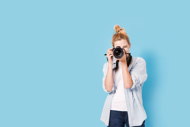 junge blonde fotografin ist fotografieren. modell isoliert auf einem blauen hintergrund mit textfreiraum - fotograf stock-fotos und bilder