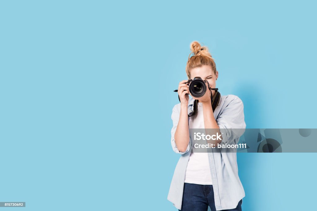 Young blonde photographer is taking a photo. Model isolated on a blue background with copy space Photographer Stock Photo