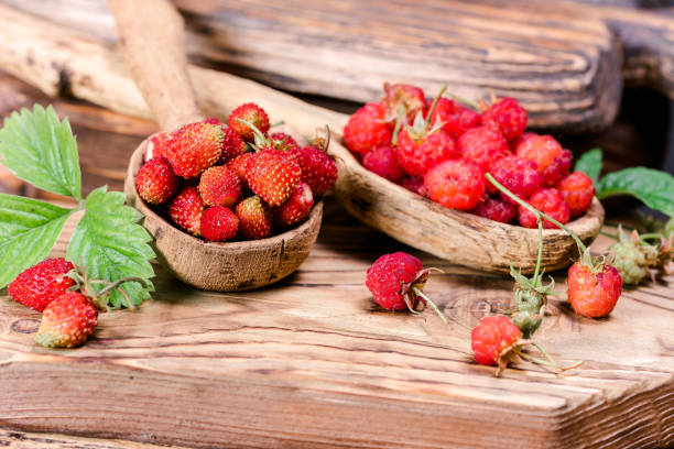Fresh raspberries and strawberries in wooden spoons on texture wood board. Close-up