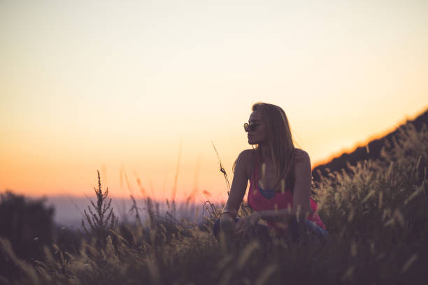 Young woman crouching in the grass field and looking at the view around her