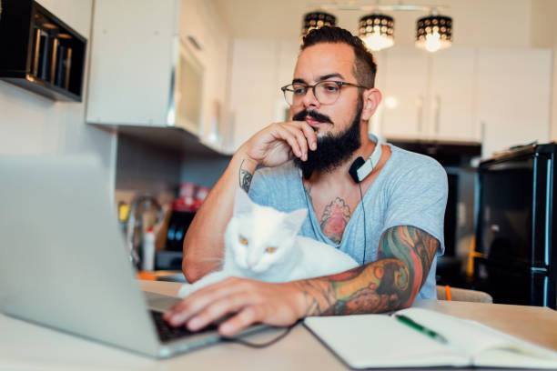 istock Man working at home on laptop with white cat next to him 815762282