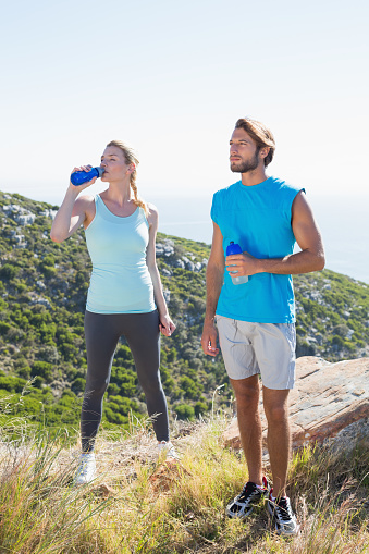 Fit couple standing drinking from water bottles on a sunny day