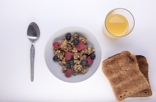 Bowl of fruit granola with orange juice and two slices of toast