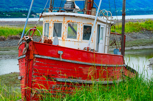 Decaying abandonded boat in a grassy field seen from walking path along the shores of Kachemak Bay in Homer Alaska.