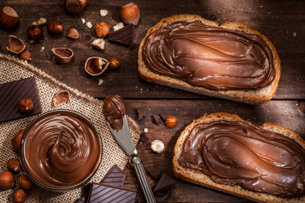 cioccolato e nocciola spalmabili su fette di pane girate su un tavolo rustico in legno - spread foto e immagini stock