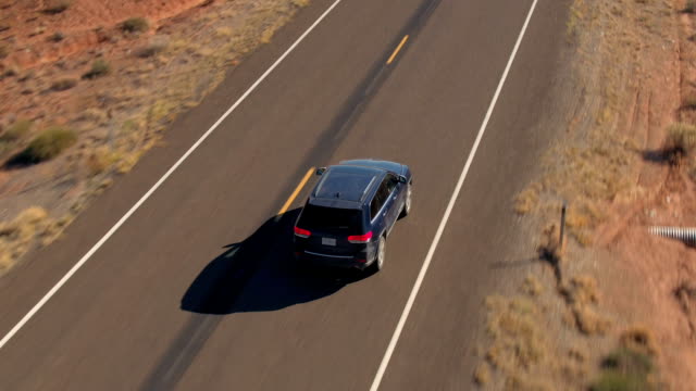 AERIAL CLOSE UP Flying above black SUV car driving on empty road in sandy desert
