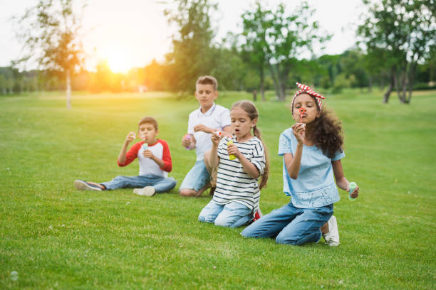 istock Cute multiethnic kids blowing soap bubbles while sitting on green lawn in park 815904188