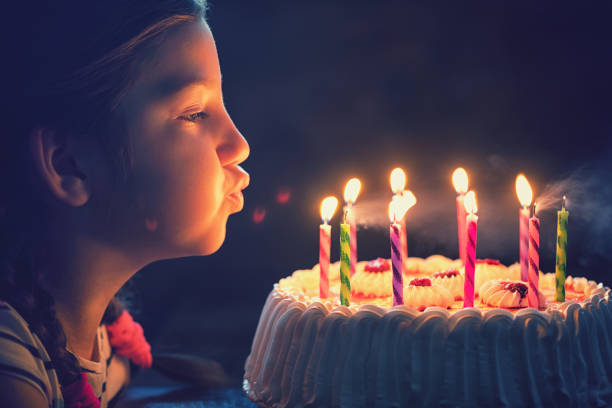 happy little girl blowing out candles on a birthday cake - little cakes imagens e fotografias de stock