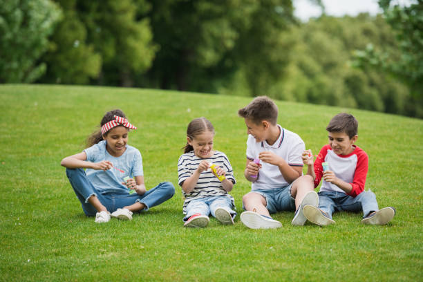 istock Happy multiethnic kids playing with soap bubbles while sitting on green meadow in park 815904486