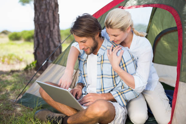 istock Attractive couple sitting by their tent using laptop 815907608