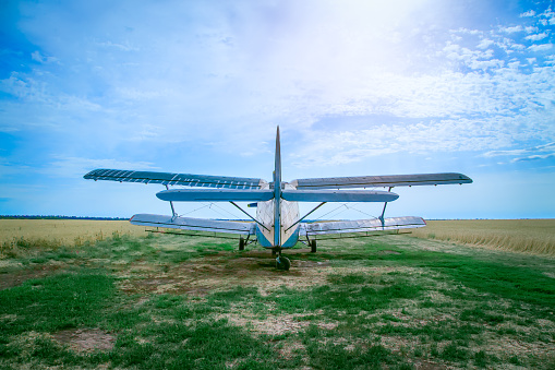 Rear view photo of an airplane. It stands on a wheat field. Blue cloudy sky is in the background.