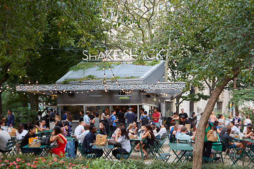 New York - September 10, 2016: Shake Shack restaurant in Madison Square Park with people sitting, outdoor tables in summer in New York. It is an American fast casual restaurant chain started in 2004 as a food cart.