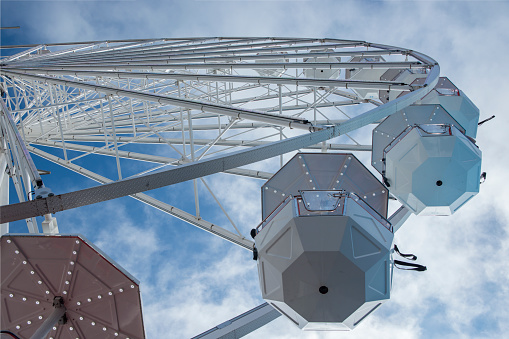 Ferris wheel photographed from below against a blue sky with soft clouds.