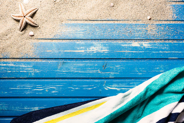 Striped towel on blue weathered wooden paltform. Beach sand and starfish on platform.