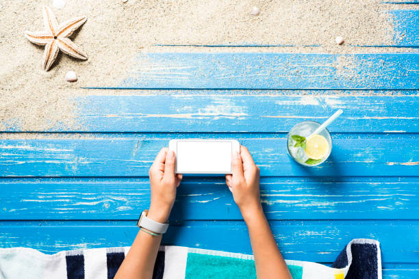 istock Woman hands holding blank screen smart phone on beach towel 816025532