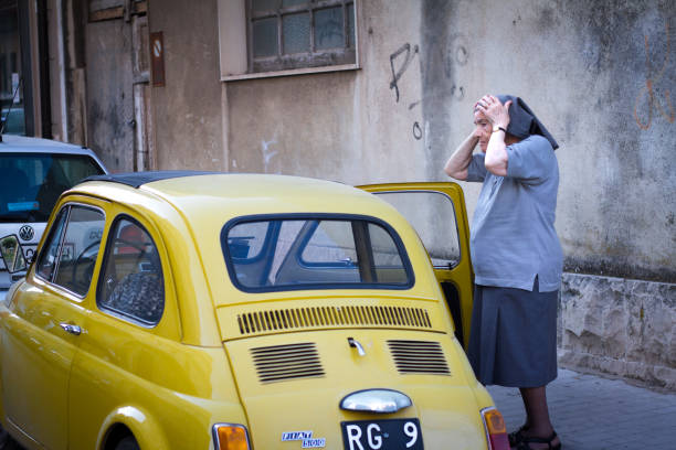 ragusa, sicilia: monja ajusta el velo cerca de amarillo vintage fiat 500 - sicily fiat old car fotografías e imágenes de stock