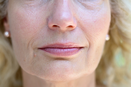 Lower face portrait of an attractive blond senior lady with a quiet smile in a concept of ageing, wrinkles, beauty and skincare