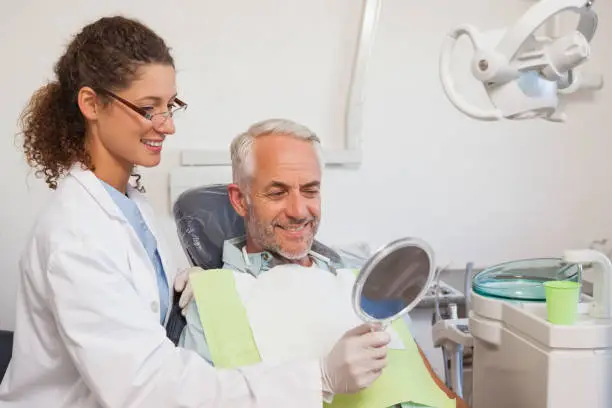 Dentist showing patient his new smile in the mirror at the dental clinic