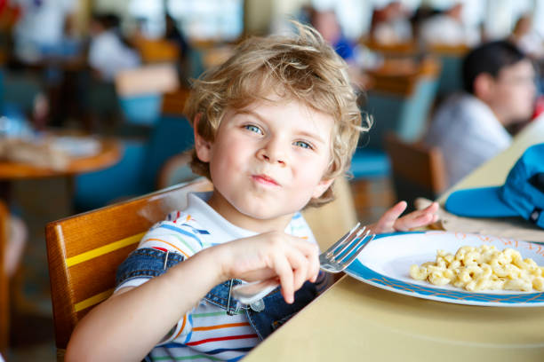 süße gesunde vorschule junge isst nudeln sitzen in schulküche - kartoffelknödel essen stock-fotos und bilder