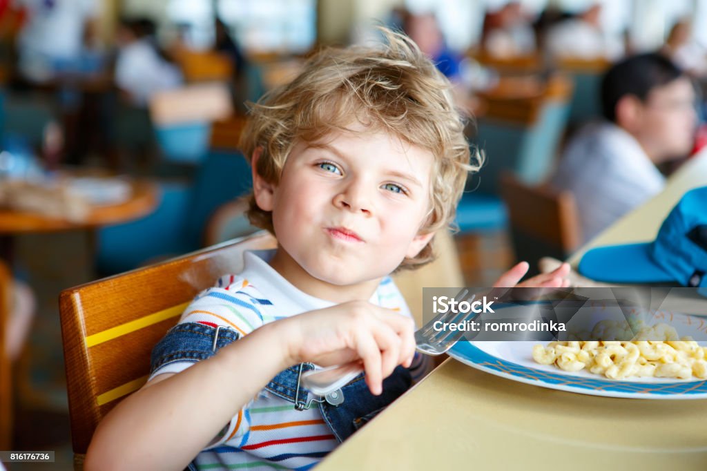 Cute healthy preschool boy eats pasta sitting in school canteen Cute healthy preschool kid boy eats pasta noodles sitting in school or nursery cafe. Happy child eating healthy organic and vegan food in restaurant. Childhood, health concept Cafeteria Stock Photo