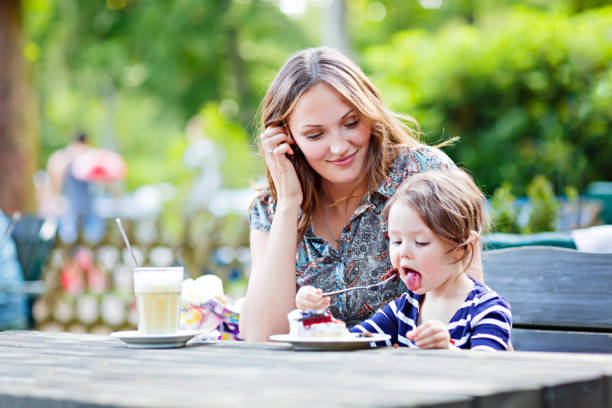 Mother and little adorable kid girl drinking coffee in cafe
