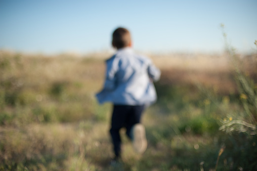 back of little boy running among the grass in blurred focus