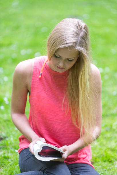 istock Young blonde woman reading a book on grass in park 816184996