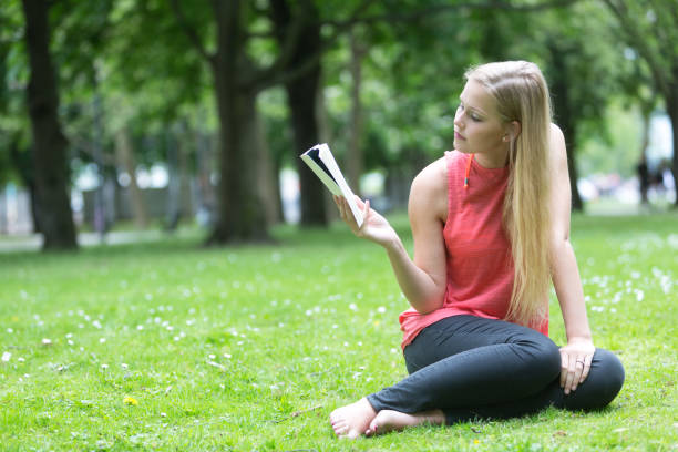 istock Young blonde girl sitting on grass in park reading a book 816185254