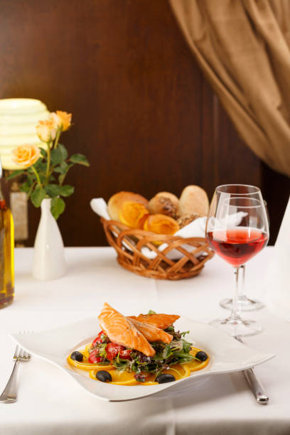 Salmón con verduras dispuestas en un plato, botella de vino y Copa de vino en segundo plano, tradicional plato en elegante entorno, enfoque selectivo con la luz suave - foto de stock