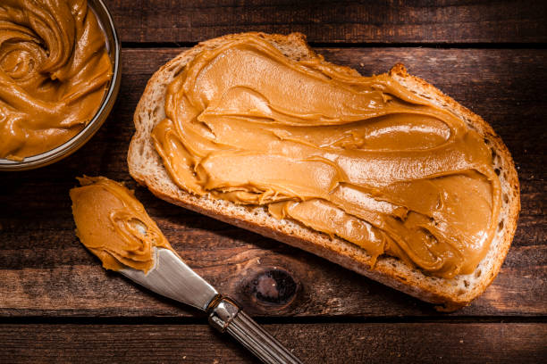 mantequilla de maní en rebanada de pan en mesa de madera rústica - peanut butter fotografías e imágenes de stock