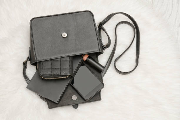 istock Open black bag with dropped things, notebook, mobile phone, purse. The white fur on background, top view. fashion concept 816246736