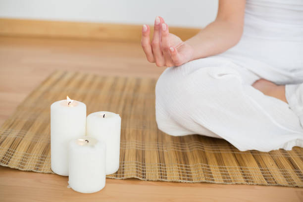 istock Woman sitting in lotus pose beside white candles 816273744