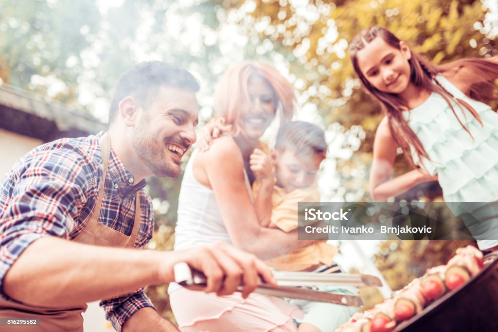 Happy young family barbecuing meat on the grill Happy family having a barbecue in their garden in summer.Leisure, food, family and holidays concept. Barbecue - Meal Stock Photo