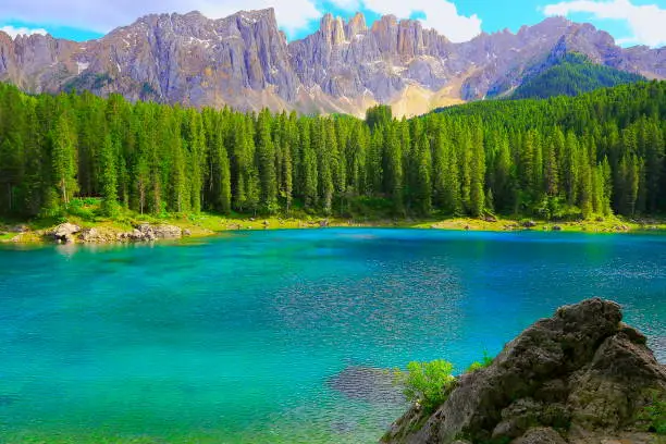 Alpine Turquoise Carezza lake (Lago di Carezza or Karersee), idyllic landscape near majestic Latemar Massif alps valley, dramatic Italian South Tirol Dolomites Snowcapped mountain range panorama, Italy