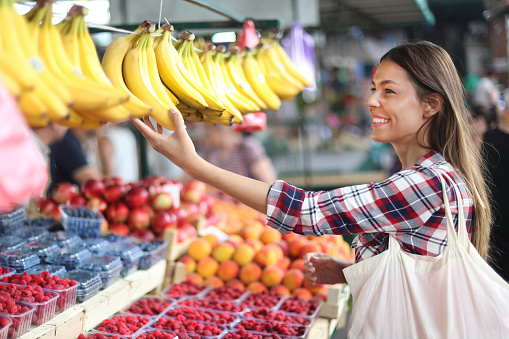 Young beautiful woman choosing fruit at a farmer's market. About 25 years old, smiling Caucasian brunette.