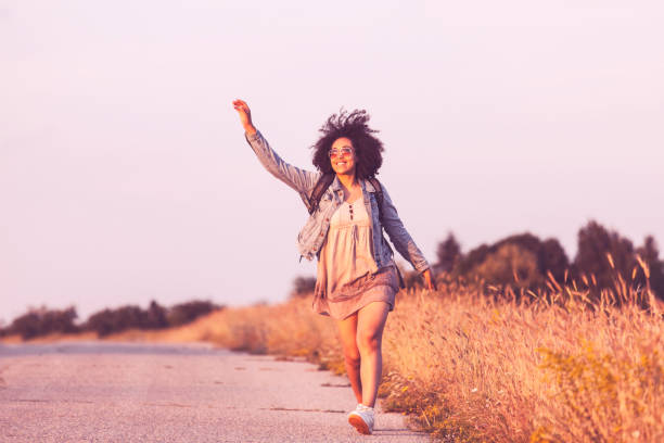 Young african woman dancing on country road, at sunset.