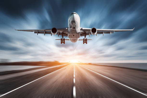 airplane and road with motion blur effect at sunset. landscape with passenger airplane is flying over the asphalt road and cloudy sky. commercial plane is landing. aircraft with blurred background - airplane taking off sky commercial airplane imagens e fotografias de stock