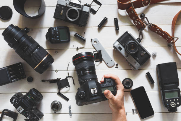 istock Man hand Holds Digital Camera On Table Next To Lenses And Accessories On White Wooden Background. Top View 816371882