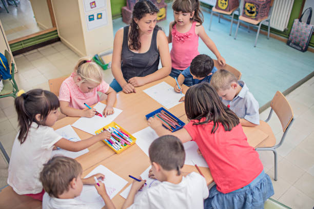 istock Teacher helping school children in drawing at desk 816391414