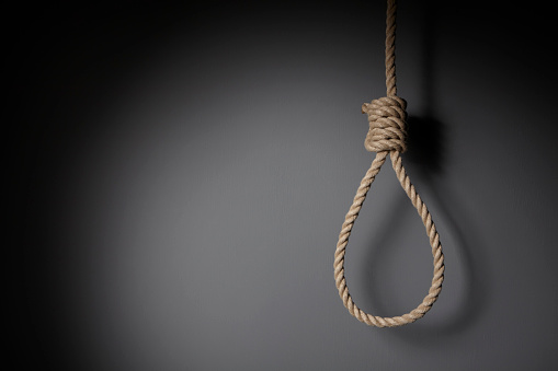 The hangman's noose is a well-known knot with its use in hanging a person. The rope is in front of a dark wall.