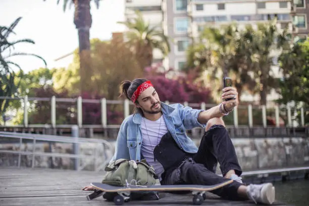 Young skateboarder taking a selfie while sitting in the city park