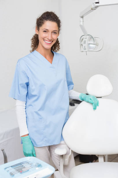 istock Dentist in blue scrubs smiling at camera beside chair 816446586