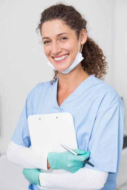 istock Dentist in blue scrubs smiling at camera holding clipboard 816452900