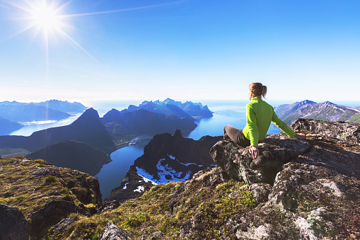 Woman hiker relaxing at the top of the mountain and looking at incredible views of a  Norwegian fjord on Senja Island, northern Norway