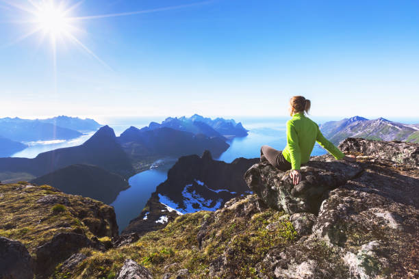 Hiker on top of mountain with view of norwegian fjord Woman hiker relaxing at the top of the mountain and looking at incredible views of a  Norwegian fjord on Senja Island, northern Norway senja island photos stock pictures, royalty-free photos & images