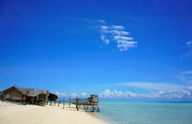 A serene coastal village with charming houses, a pebble beach, and dramatic clouds overhead. A paddle boarder adds a sense of adventure to the peaceful scene.