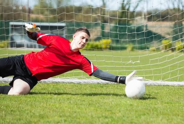 вратарь в красном спасает гол во время игры - goalie soccer soccer player teenage boys стоковые фото и изображения